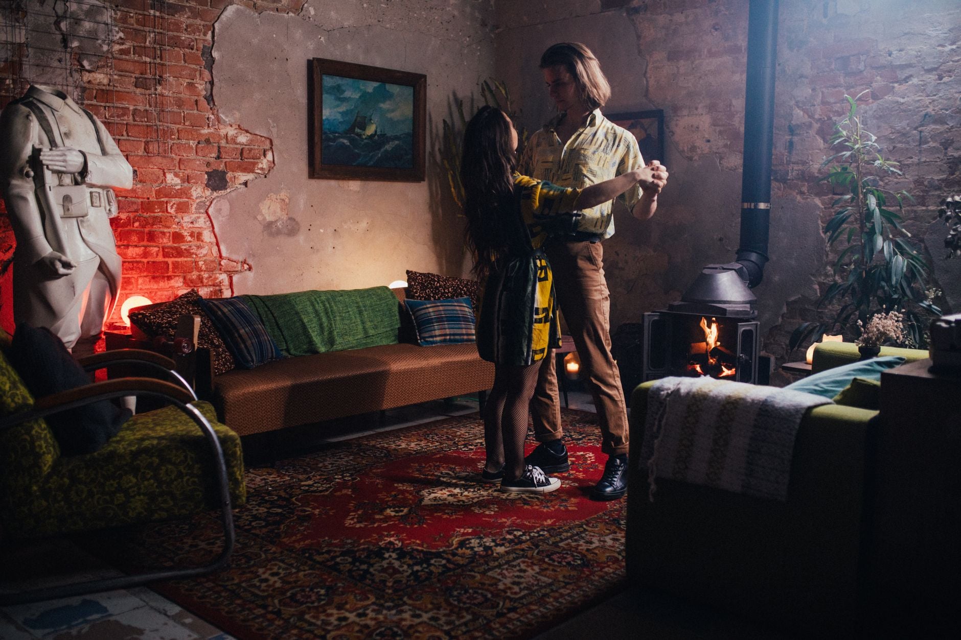 A couple dances happily in a cozy, art-decorated indoor space with warm lighting.